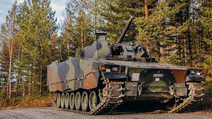 BAE Systems Hagglunds' CV9030 in camo paint positioned on a gravel road next to an evergreen forest